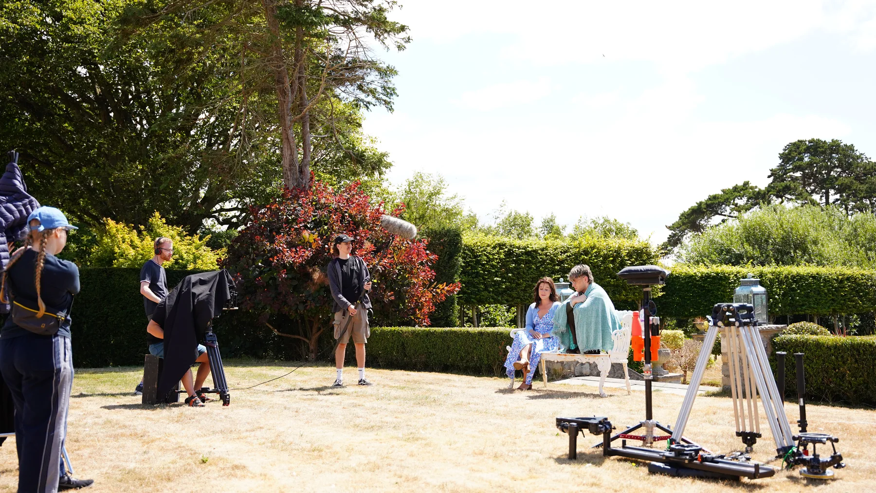 Outdoor filming setup with cast, crew and camera equipment on a lawn