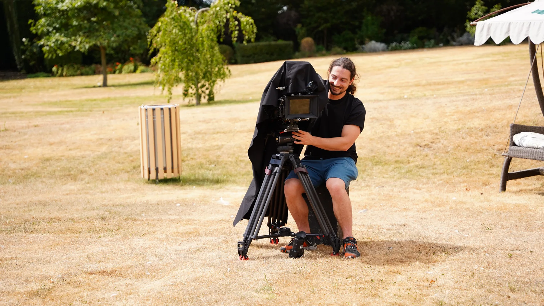 Camera operator filming from a tripod on the lawn