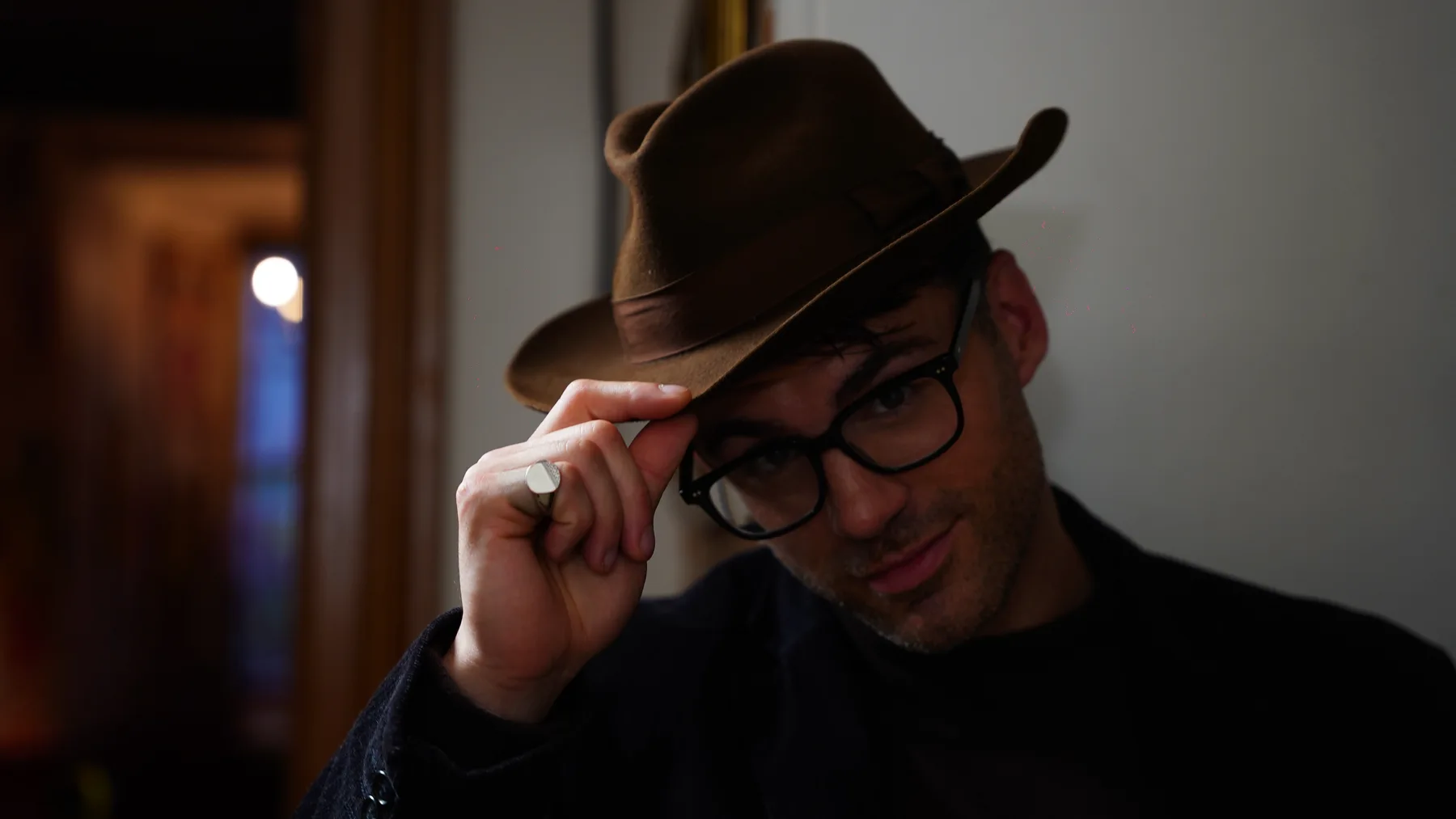 Actor in a hat lifting the brim in character