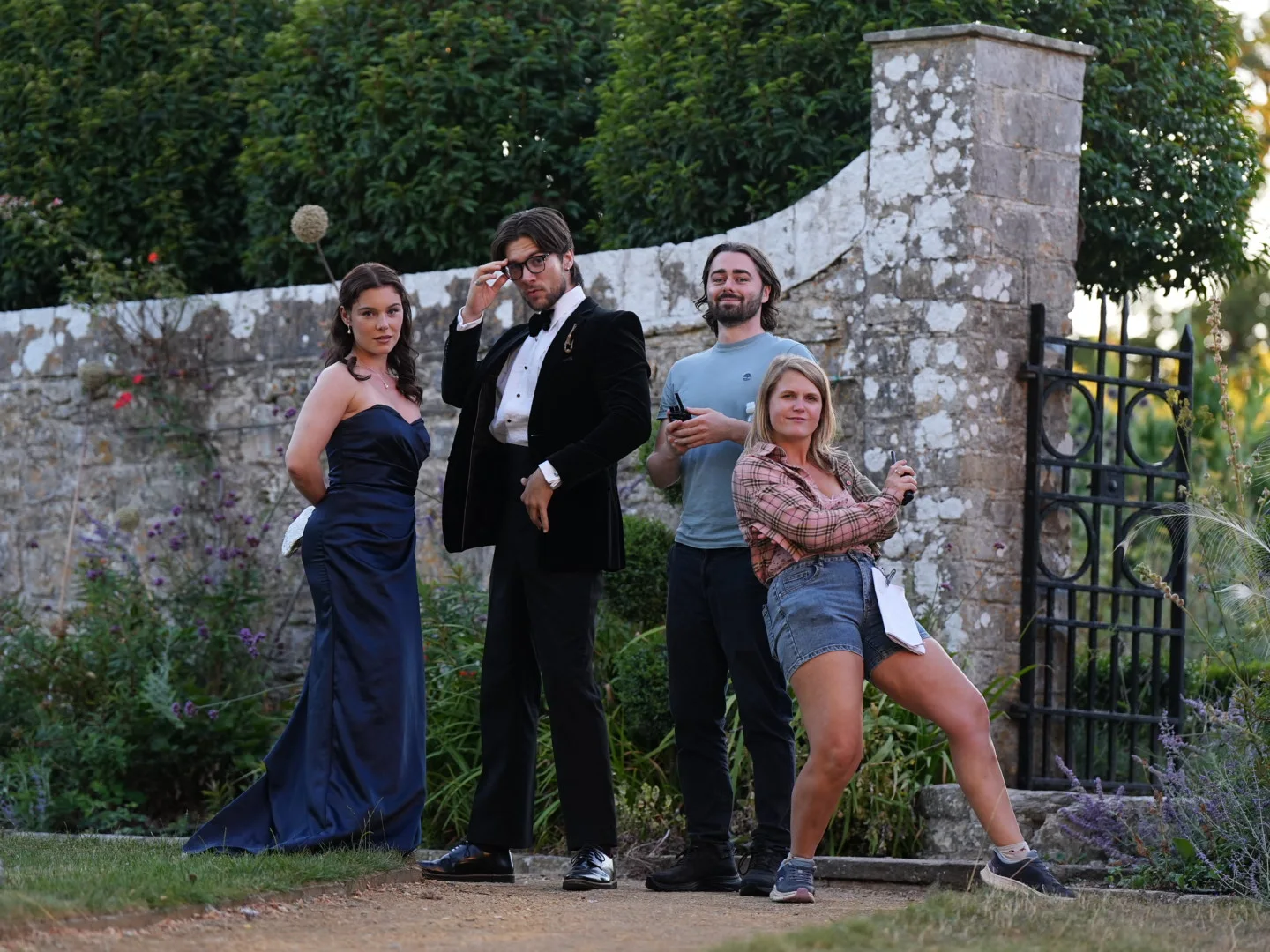 Cast and crew posing together beside a garden gate