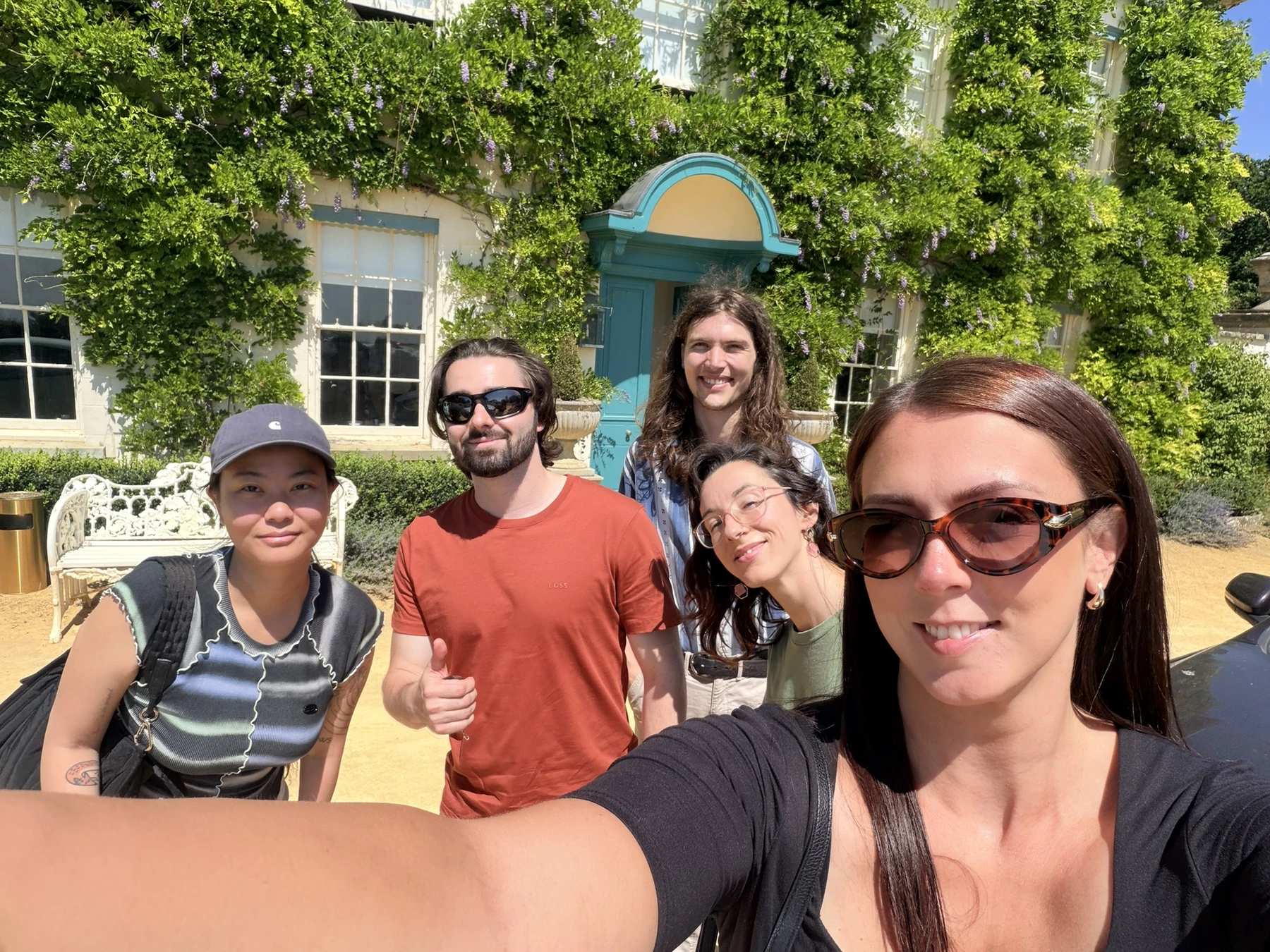 Five team members taking a group selfie outside the ivy-covered manor