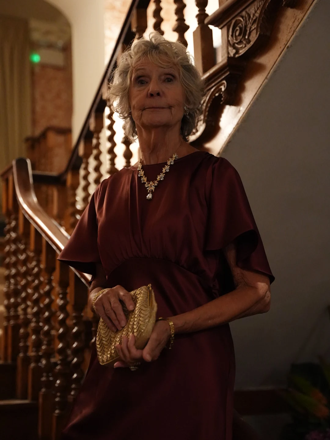 Judith Haley in a burgundy dress standing beside a staircase
