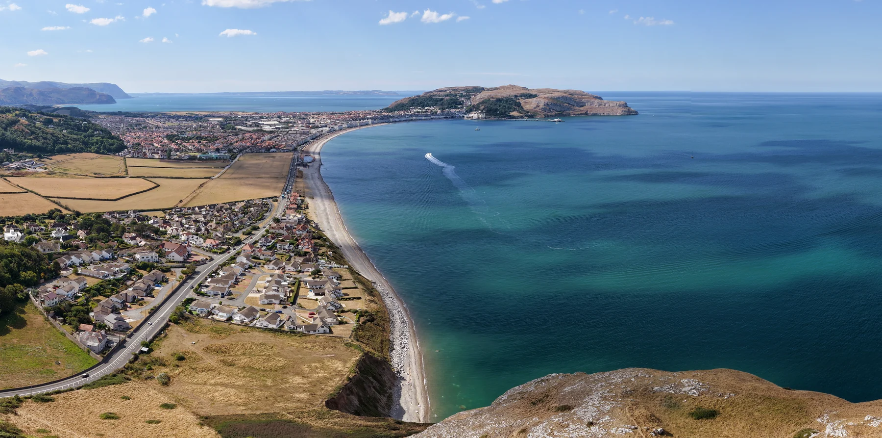 Aerial view of Llandudno Bay, its coastline and a boat trail across the sea